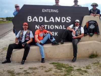 Seven motorcyclists sit on the signboard Badlands National Park